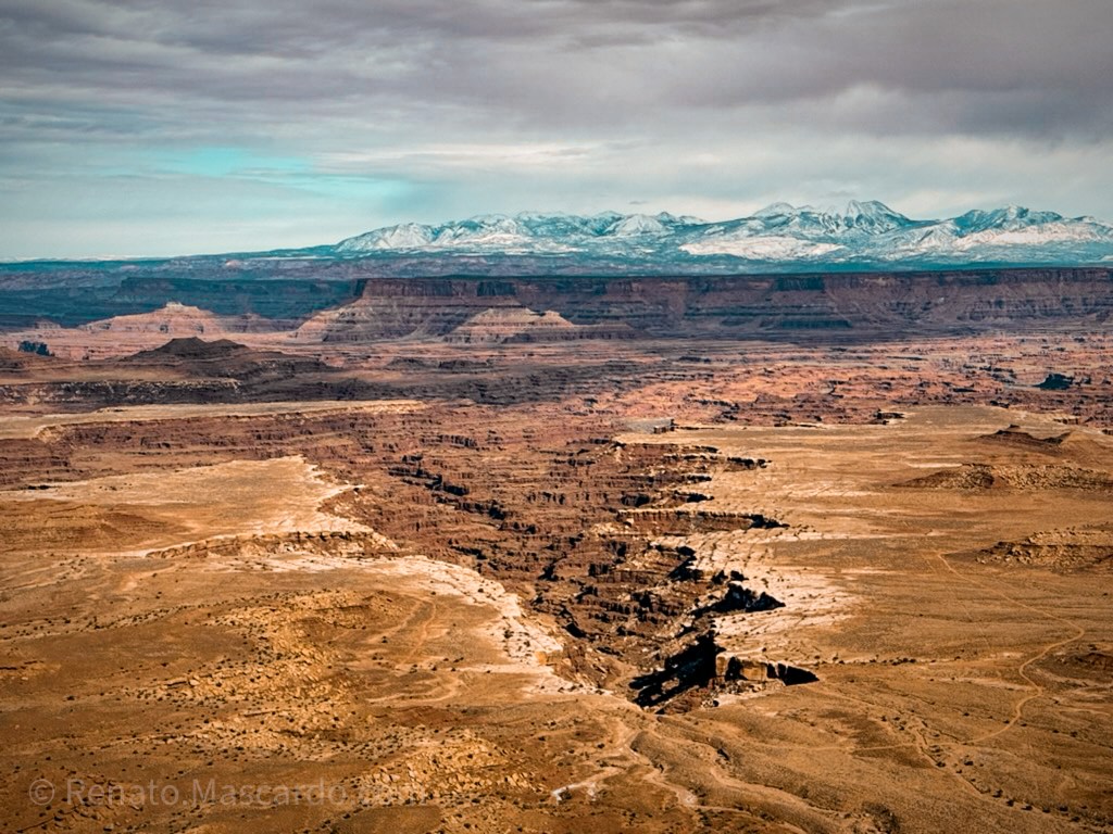 A sweeping view of rugged canyons and distant mountains under a dramatic sky in Canyonlands National Park, Utah.