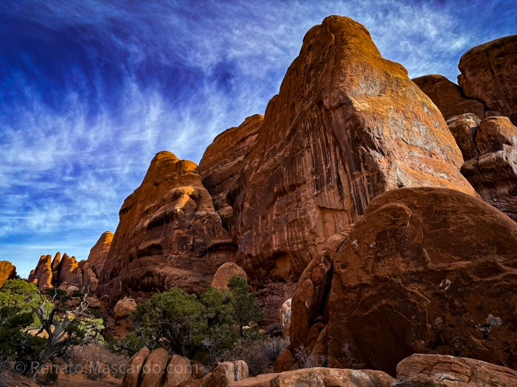 A scenic view of towering red rock formations against a blue sky with wispy clouds, showcasing the dramatic landscape of Arches National Park.