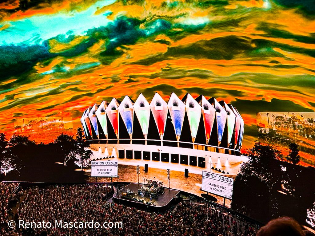 A vibrant image of the Hampton Coliseum featuring the Grateful Dead in concert, with a colorful, dramatic sky in the background and a large crowd gathered in front.