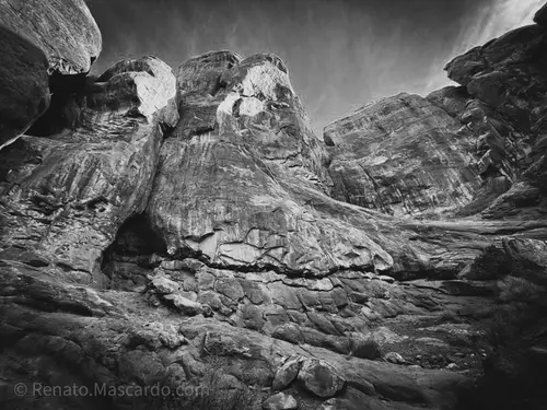 A black and white image of towering rock formations and textured cliffs, showcasing the rugged landscape of a canyon.