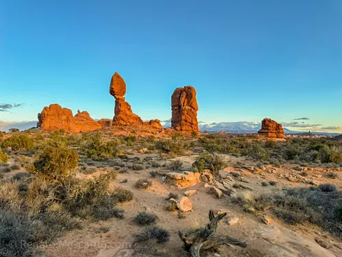 A panoramic view of Arches National Park featuring unique rock formations and a clear blue sky during sunset.