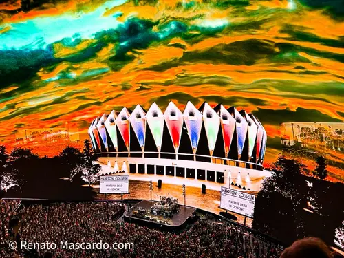 A vibrant image of the Hampton Coliseum featuring the Grateful Dead in concert, with a colorful, dramatic sky in the background and a large crowd gathered in front.